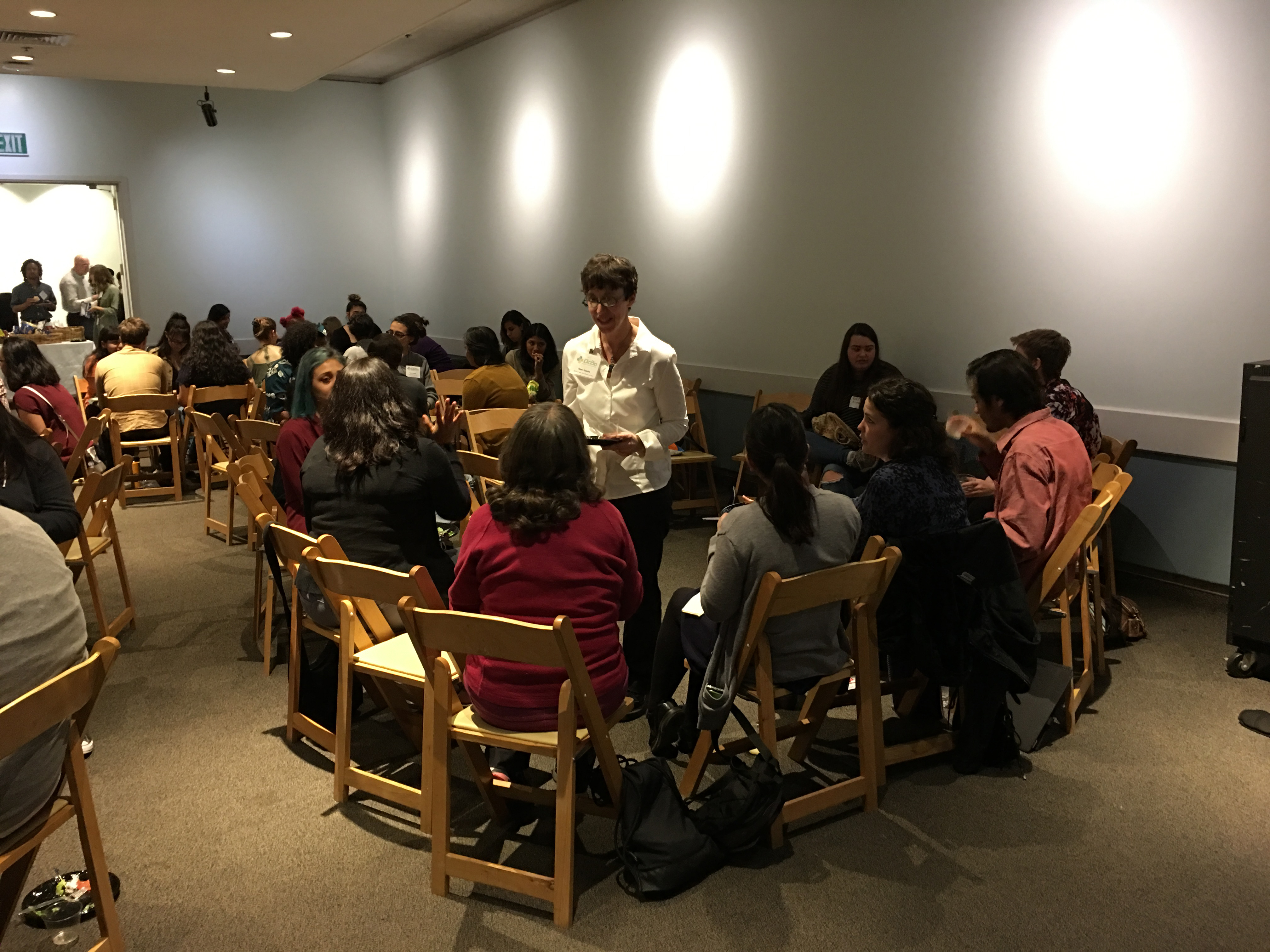 Mare Nazaire talks with workshop participants during lunch. Image shows a large group of people in a room talking and eating lunch.