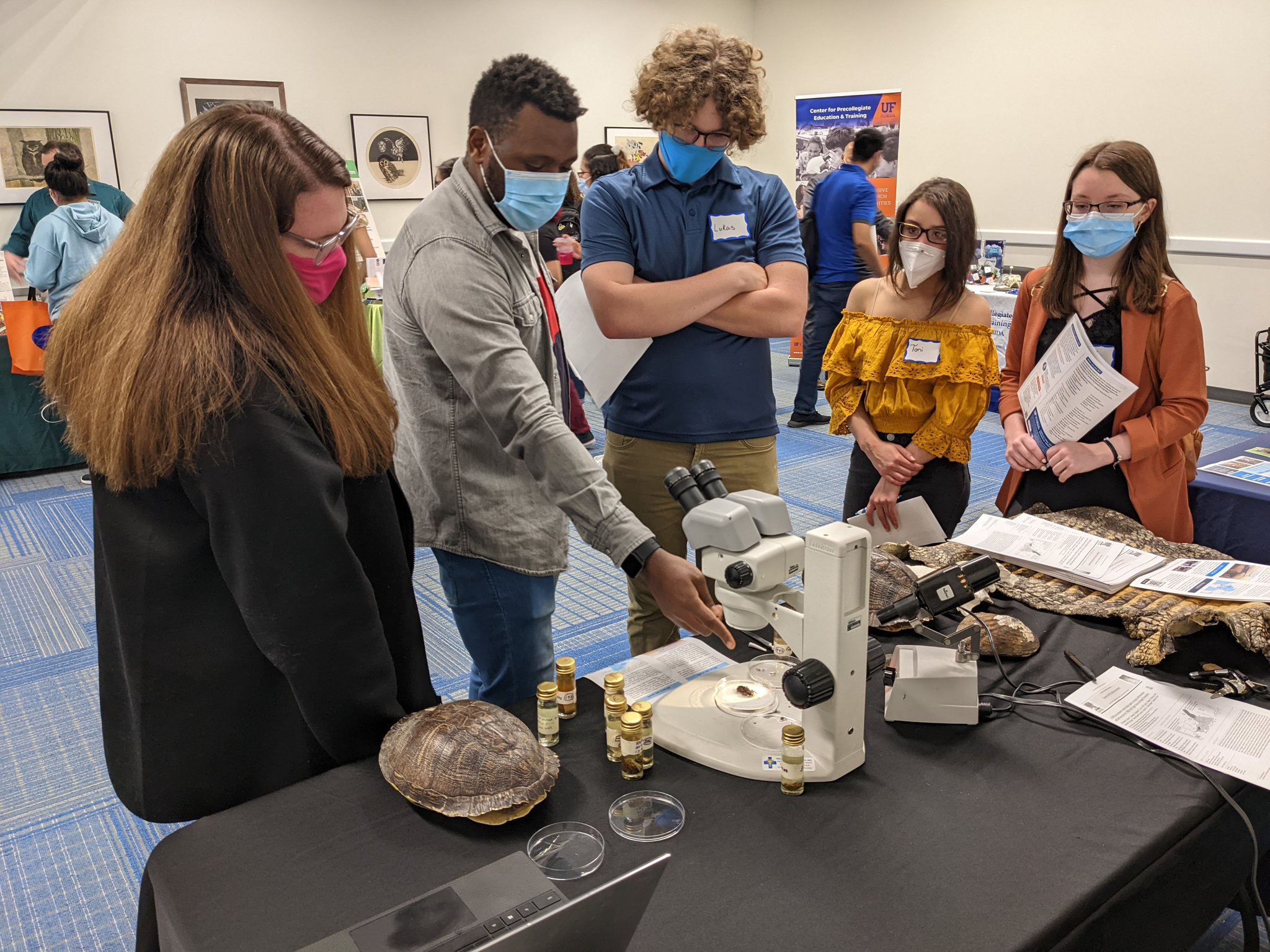 4 students look at specimens and a microscope at the tabling event. 